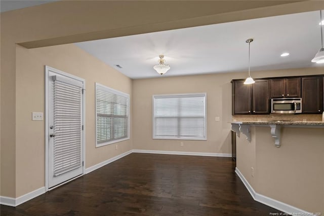 kitchen with decorative backsplash, stainless steel microwave, dark wood-style flooring, and dark brown cabinetry