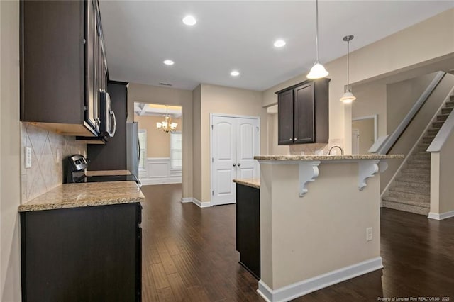 kitchen featuring light stone counters, a kitchen breakfast bar, range with electric stovetop, dark wood finished floors, and a peninsula