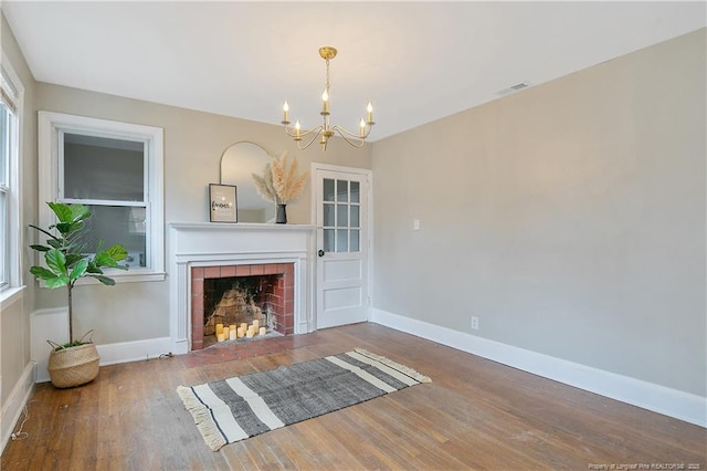 unfurnished living room featuring a notable chandelier, a tile fireplace, visible vents, and wood finished floors