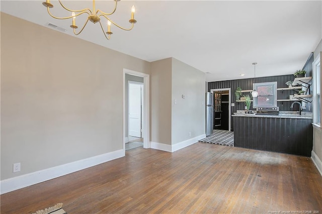 unfurnished living room with visible vents, wood-type flooring, baseboards, and a chandelier