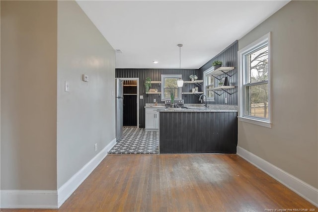 kitchen with open shelves, wood finished floors, freestanding refrigerator, baseboards, and hanging light fixtures