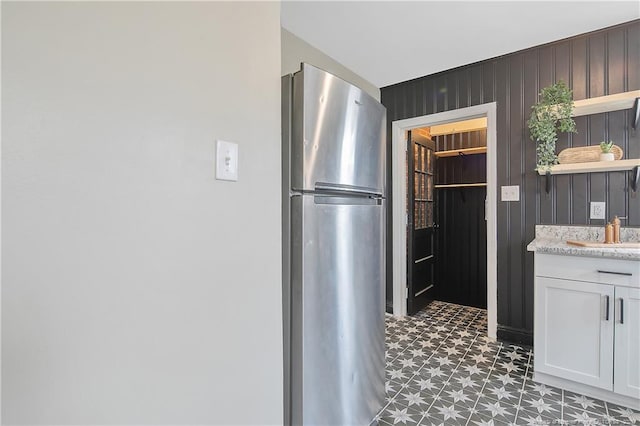 kitchen featuring light floors, wood walls, freestanding refrigerator, white cabinetry, and open shelves