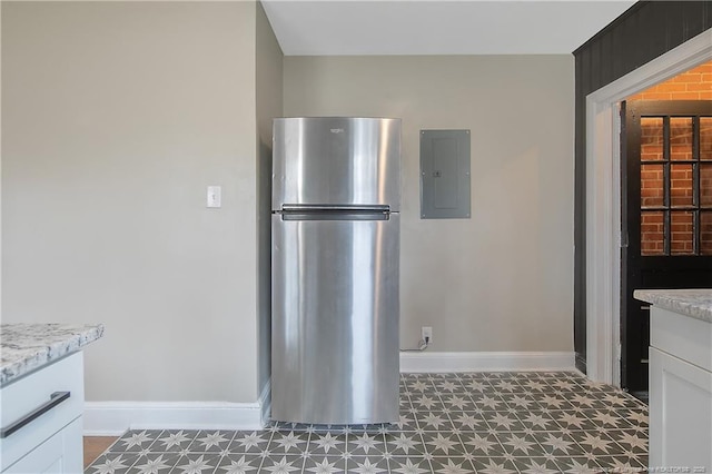 kitchen featuring baseboards, electric panel, freestanding refrigerator, tile patterned floors, and white cabinetry