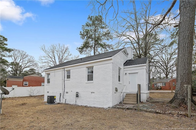 rear view of property featuring brick siding, roof with shingles, and fence