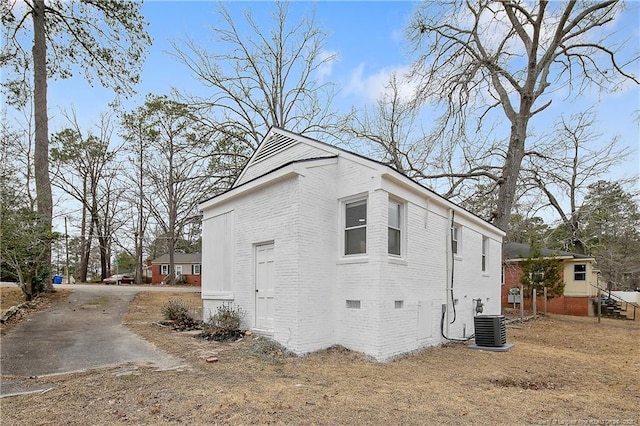 view of home's exterior with cooling unit, brick siding, driveway, and crawl space