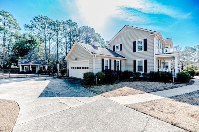 traditional-style home with a balcony, driveway, a porch, an attached garage, and a chimney