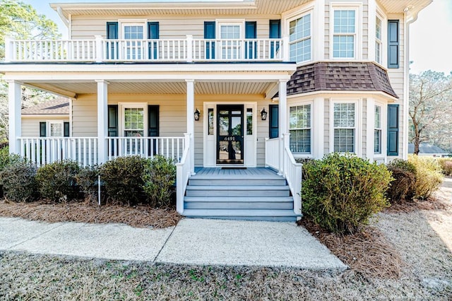 doorway to property featuring covered porch and roof with shingles