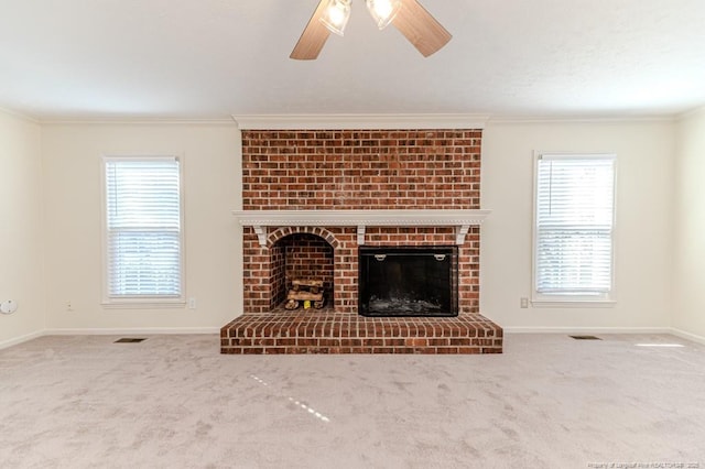 unfurnished living room with a brick fireplace, crown molding, ceiling fan, and carpet floors