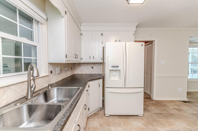 kitchen featuring dark countertops, decorative backsplash, white fridge with ice dispenser, white cabinets, and a sink