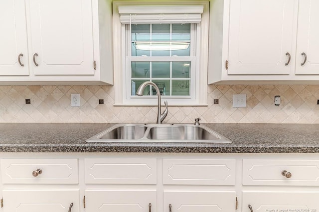 kitchen with dark countertops, white cabinetry, and a sink