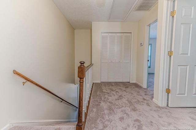 hall with carpet, visible vents, attic access, a textured ceiling, and an upstairs landing