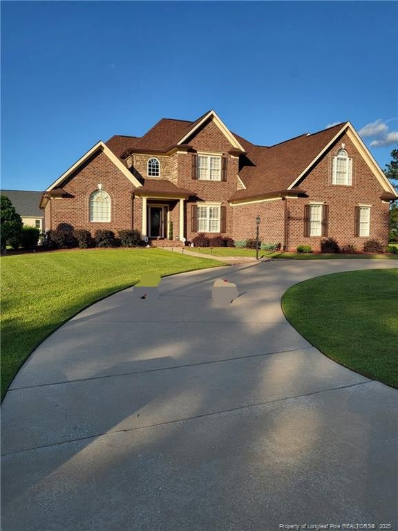 view of front facade featuring brick siding, curved driveway, and a front yard