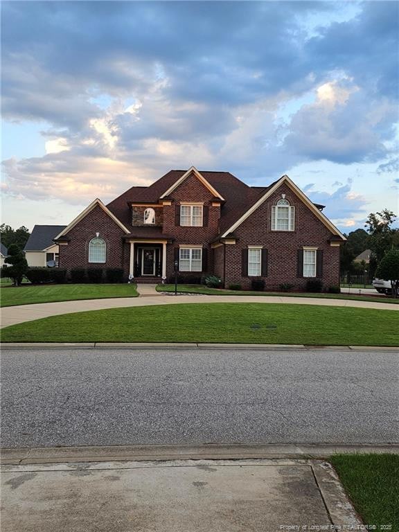 view of front facade with a front yard, brick siding, and curved driveway