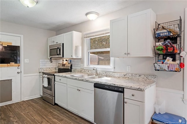 kitchen with dark wood finished floors, a sink, white cabinets, appliances with stainless steel finishes, and a textured ceiling