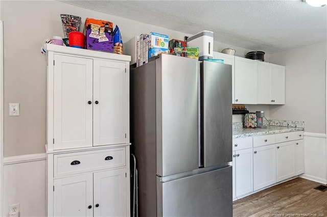 kitchen with wainscoting, freestanding refrigerator, wood finished floors, a textured ceiling, and white cabinetry