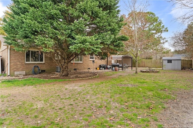 view of yard featuring fence, a shed, central air condition unit, an outdoor fire pit, and an outdoor structure