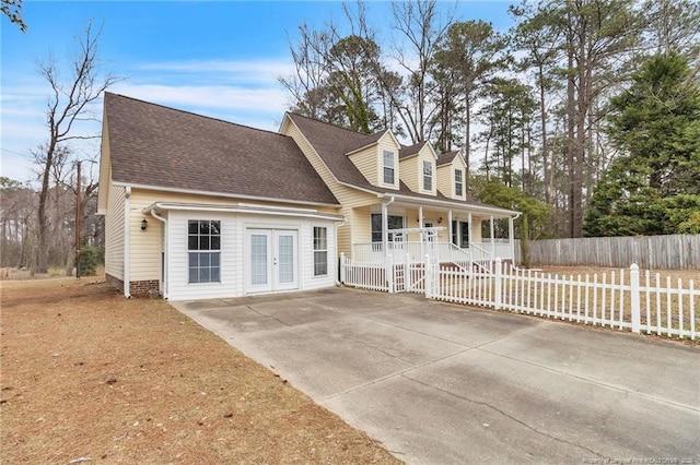 new england style home with a porch, a shingled roof, french doors, and fence