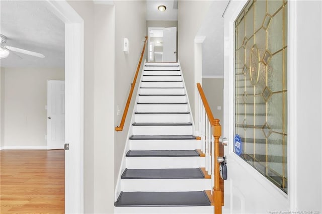 stairway with baseboards, wood finished floors, and a ceiling fan