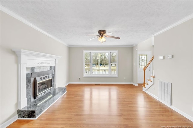 unfurnished living room with visible vents, ceiling fan, stairway, a premium fireplace, and light wood-style flooring