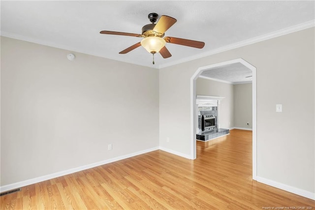 empty room featuring light wood-type flooring, visible vents, a ceiling fan, a tiled fireplace, and crown molding