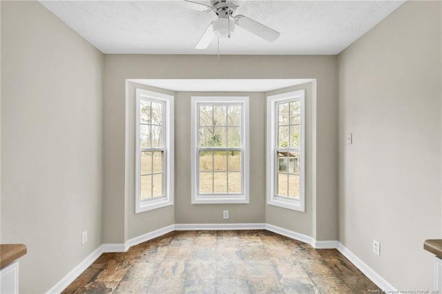 empty room with baseboards, a textured ceiling, a ceiling fan, and stone finish floor