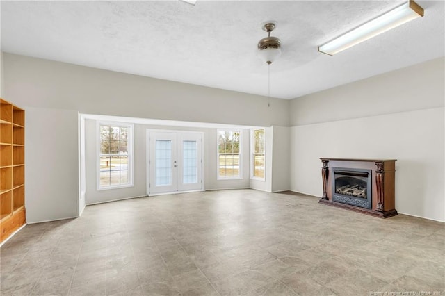 unfurnished living room with a healthy amount of sunlight, a fireplace, a textured ceiling, and french doors