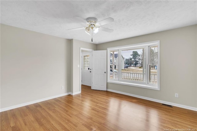 spare room with a textured ceiling, baseboards, visible vents, and light wood-type flooring