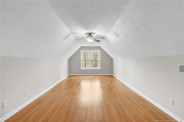 bonus room with light wood-type flooring, visible vents, a textured ceiling, baseboards, and ceiling fan