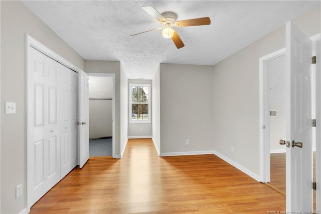 unfurnished bedroom with baseboards, ceiling fan, light wood-style floors, a closet, and a textured ceiling