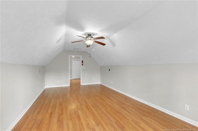 bonus room with a textured ceiling, light wood-style floors, baseboards, ceiling fan, and vaulted ceiling