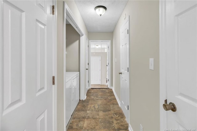 hallway featuring washing machine and clothes dryer, a textured ceiling, baseboards, and stone finish flooring