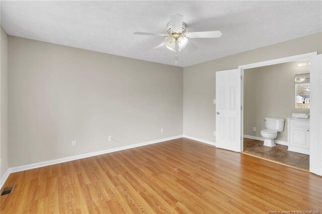 unfurnished bedroom featuring connected bathroom, baseboards, visible vents, and light wood-type flooring