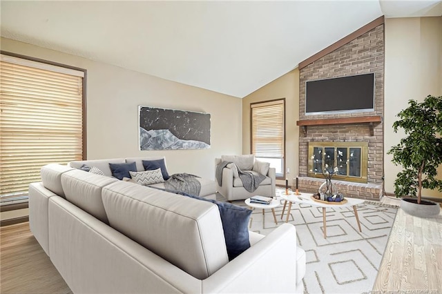 living area featuring lofted ceiling, a brick fireplace, and light wood finished floors