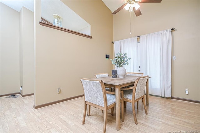 dining space with a ceiling fan, baseboards, light wood finished floors, and high vaulted ceiling