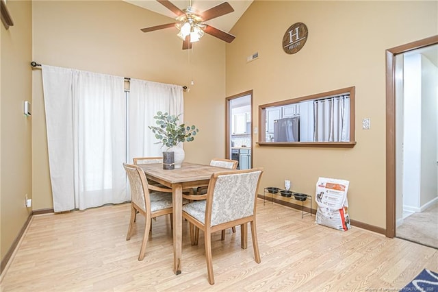 dining space featuring visible vents, baseboards, light wood-style floors, high vaulted ceiling, and a ceiling fan