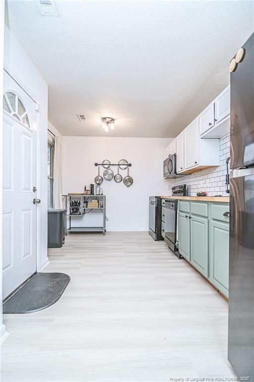 kitchen with black microwave, light wood-type flooring, decorative backsplash, freestanding refrigerator, and range