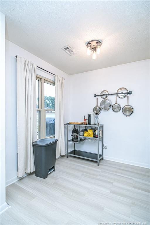 interior space featuring visible vents, a textured ceiling, baseboards, and wood finished floors