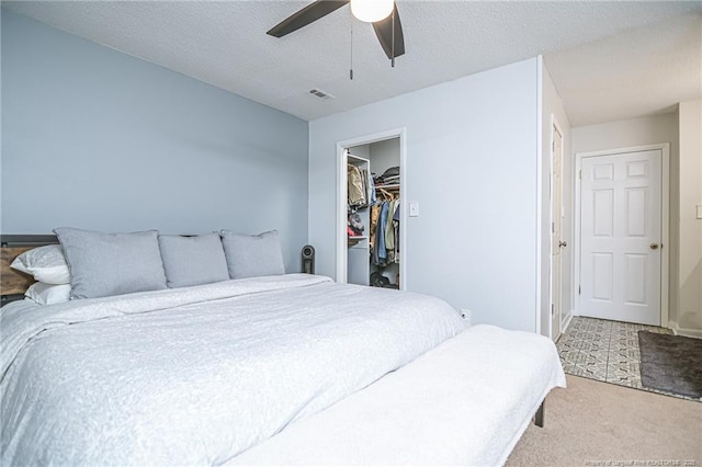 carpeted bedroom with a ceiling fan, visible vents, a spacious closet, a closet, and a textured ceiling