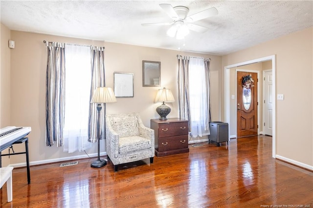 living area with baseboards, a textured ceiling, a ceiling fan, and wood finished floors