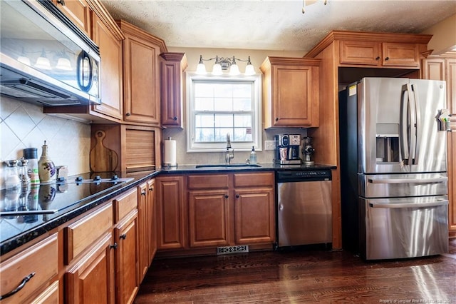 kitchen featuring a sink, appliances with stainless steel finishes, brown cabinetry, decorative backsplash, and dark wood-style flooring