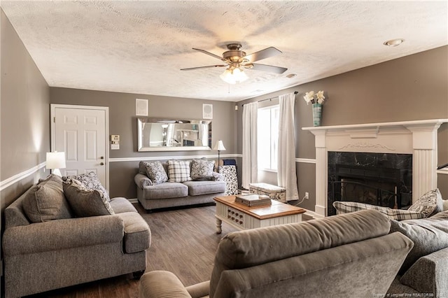 living area with a high end fireplace, baseboards, ceiling fan, wood finished floors, and a textured ceiling