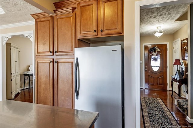 kitchen with brown cabinets, a textured ceiling, dark wood-style floors, and freestanding refrigerator