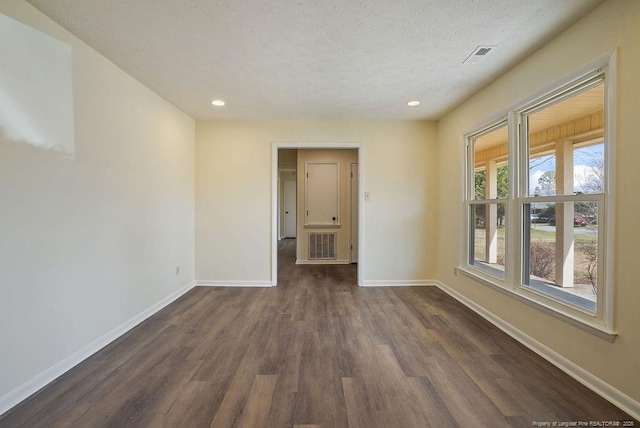 spare room with dark wood-type flooring, visible vents, baseboards, and a textured ceiling