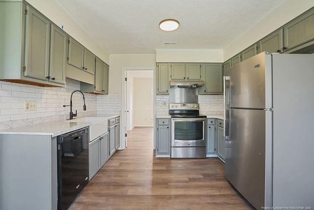 kitchen featuring green cabinets, under cabinet range hood, light countertops, appliances with stainless steel finishes, and dark wood-style flooring