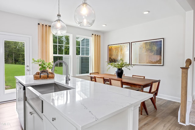 kitchen with light stone countertops, baseboards, a sink, hanging light fixtures, and light wood-style floors