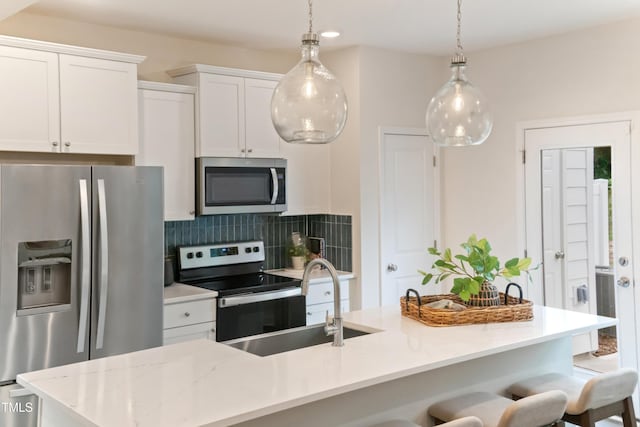 kitchen with a kitchen bar, decorative light fixtures, tasteful backsplash, white cabinetry, and stainless steel appliances