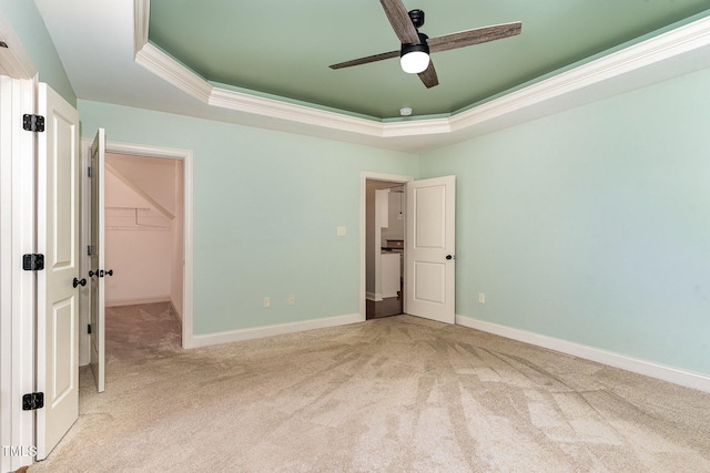 unfurnished bedroom with carpet flooring, a walk in closet, a raised ceiling, baseboards, and ornamental molding