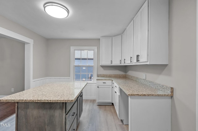 kitchen with light stone counters, a kitchen island, white cabinets, light wood-style floors, and wainscoting