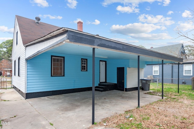 rear view of house with fence, a carport, a chimney, and entry steps