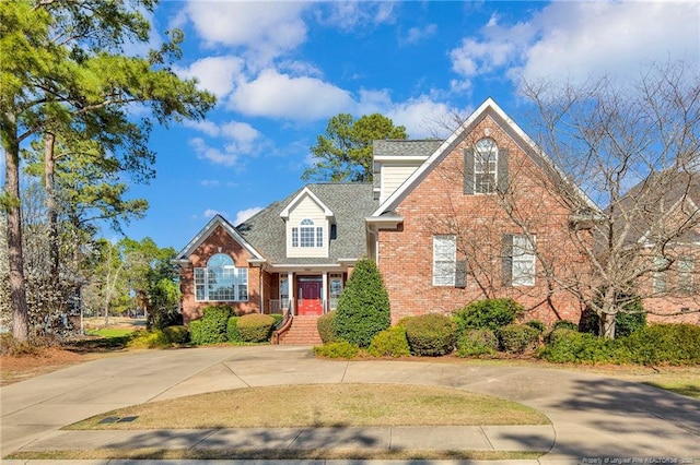 traditional-style home featuring brick siding, curved driveway, and a shingled roof